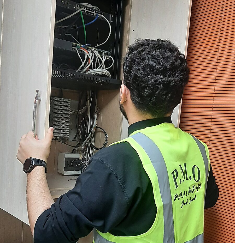 Erfan Khadiv in a Ports and Maritime Organization safety vest working on a network cabinet